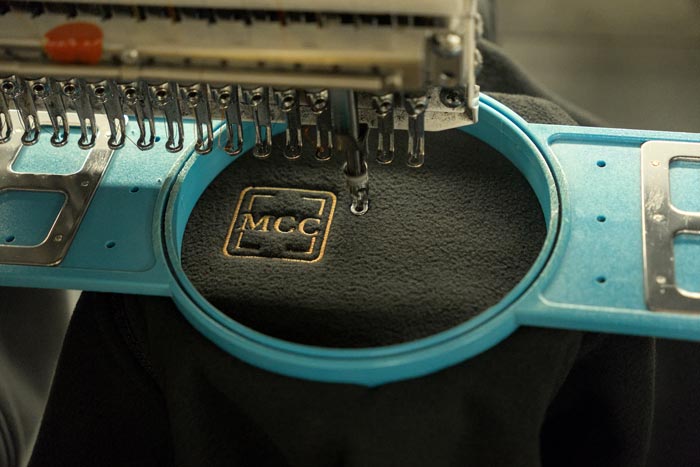 Close-up of a custom MCC logo being embroidered onto black fabric
